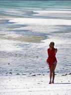 Back view of the woman in underwear and red cover, standing on the sea beach with waves