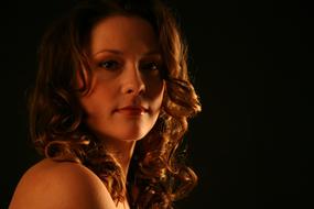 Portrait of the woman with curly hair, in light, at black background