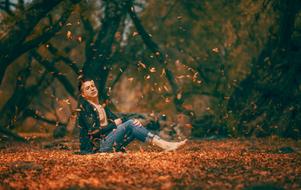 Man sitting on the ground with colorful leaves, among the forest in the autumn