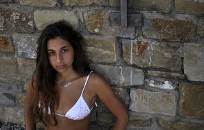 Girl in bikini standing by the stone wall