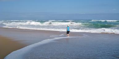 a woman walks along the sandy beach among the waves