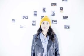 Smiling woman in jacket and yellow beanie, at background with the images