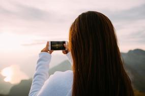 back view of long haired woman taking shot of scenic landscape