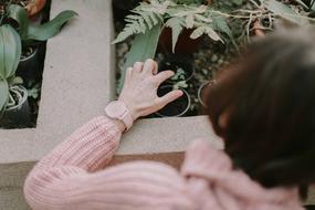 Old woman in pink sweater and with pink watch lookin on the beautiful and colorful plants