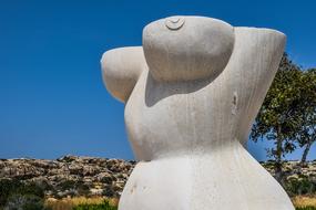 Beautiful, marble woman body sculpture, among the colorful plants, at blue sky background, in Ayia Napa, Cyprus, Greece
