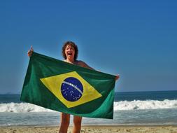happy woman holds brazilian flag on beach in front of sea