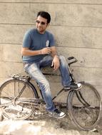 Man in glasses, with the tea, sitting on the retro bicycle, near the wall, in light