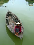 Senior asian woman in traditional boat on green water