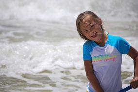 Smiling, blonde girl, on the beach, near the green water with white waves