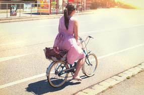 Woman in pink Dress riding bicycle on road