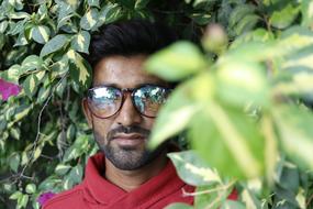 Indian student in glasses on a background of green bush