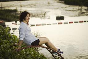 Smiling woman, sitting on the rusty construction, near the water