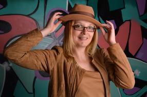 woman in brown suit and hat stands against graffiti background