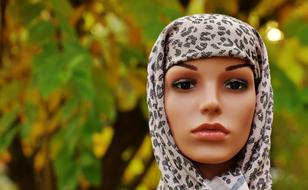 Portrait of a mannequin, covered in patterned, colorful cloth, among the colorful plants