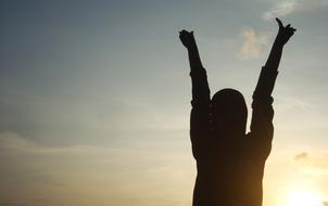 silhouette of a man with hands up against the evening sky