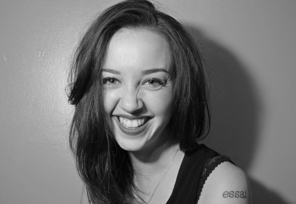 Black and white portrait of the smiling woman with tattoo, with shadow on the wall