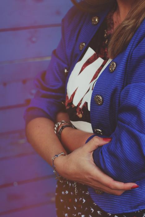 Woman in blue jacket, holding hands together, near the blue wall