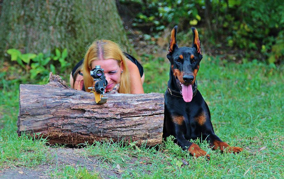 girl with guns next to the doberman