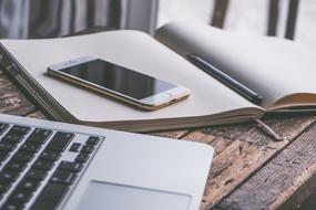 smartphone lies on a notebook and laptop on a table