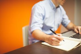 manager works on a laptop and writes data to a notebook