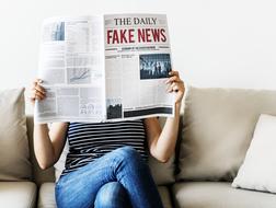 Woman, reading American newspaper, while sitting on the couch