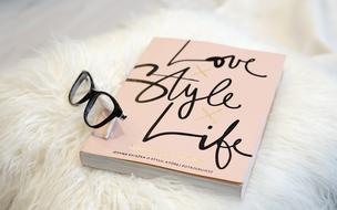 Pink and black notebook with the black glasses on white surface
