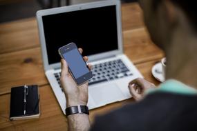 young man works on a laptop and holds a smartphone in his hand