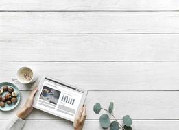 tablet in hand, sweets, a cup of coffee and a plant on the table