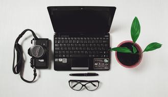 laptop, camera, glasses and a potted flower on the table