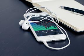 Mobile Phone with headphones and open notebook with pen on table