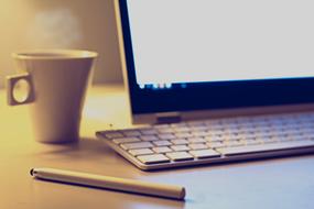 cup with hot drink, pen and computer on the table