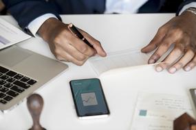 Person in suit, writing something on the paper, on the white table with devices