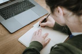 laptop on the table and the girl makes notes in the notepad