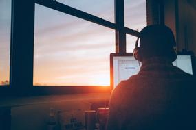 young man with headphones works at the computer by the window