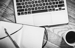 black and white photo of laptop, notebook and cup of coffee