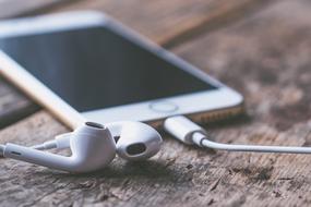 Close-up of the beautiful, shiny, white Iphone, with the white earphones, on the wooden surface