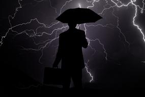 silhouette of a businessman under an umbrella on a background of a stormy sky and lightnings