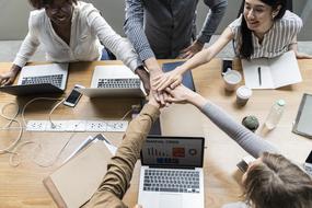 Agreement, five people holding hands together above table with laptops