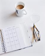 Calendar, Eyeglasses and mug with drink on desk