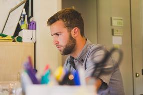 Profile portrait of the beaded man, working at the desk, with the colorful supplies