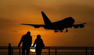 silhouette of couple and airplane taking off against orange sky