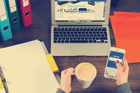 mug and phone in female hands in front of laptop computer