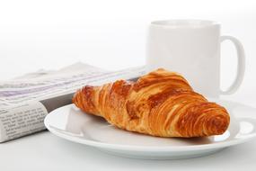 croissant on a plate, a cup of coffee and a newspaper