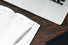 White and black notebook and shiny pen, laying on the notebook, on the wooden surface