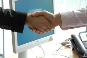 Close-up of the handshake, between the people, near the monitor and telephone