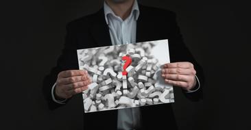 Businessman holds board with red question mark on grey ones