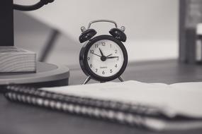 black and white photo of a notebook and an alarm clock on a table