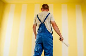 Back view of the painter in costume, near the yellow and white wall with strips