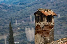 Close-up o the colorful, old chimney on the house, at background with the green trees on the landscape