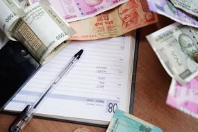 Indian Rupee bank notes and notebook with pen on desk